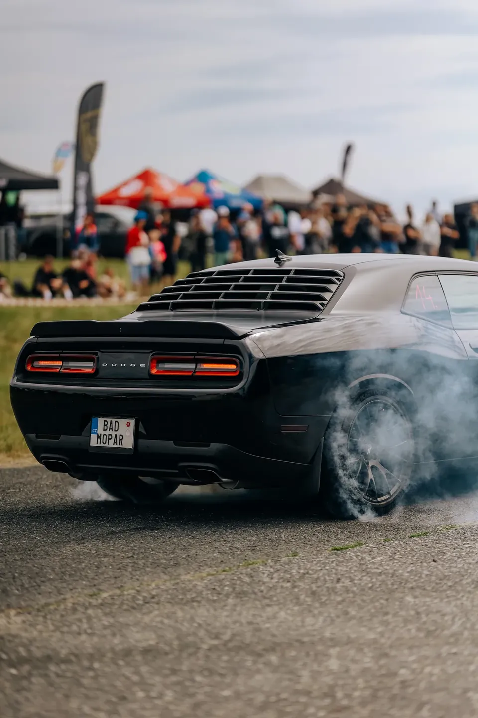Černý Dodge Challenger zezadu při burnoutu, zpod kol se valí kouř