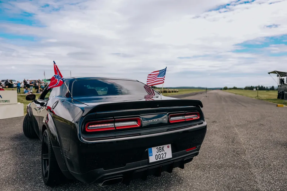 Černý Dodge Challenger zezadu s vlajkami na startu dráhy