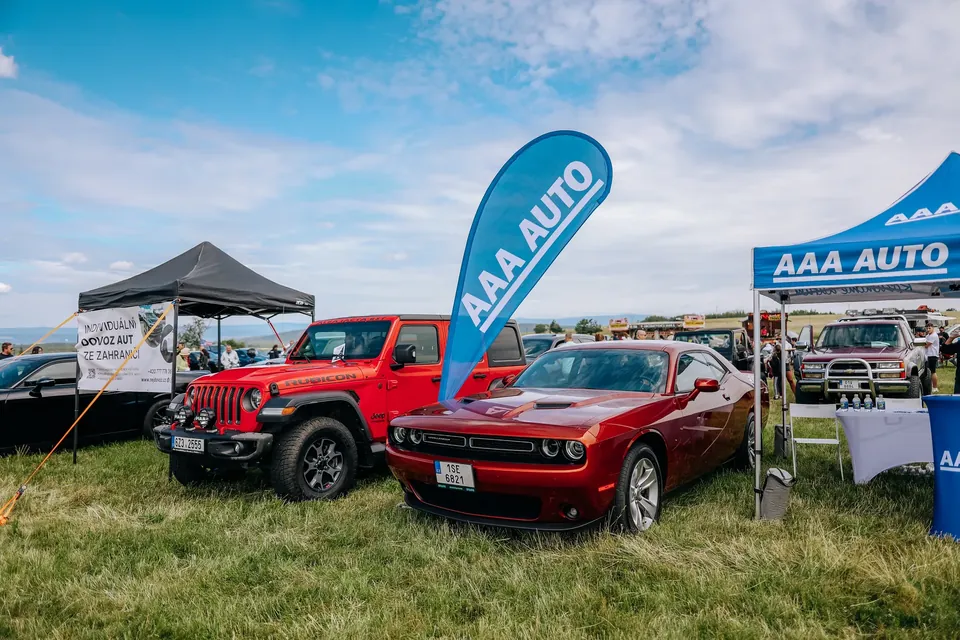 Červený Jeep Wrangler a červený Dodge Challenger na trávě u stánku AAA Auto